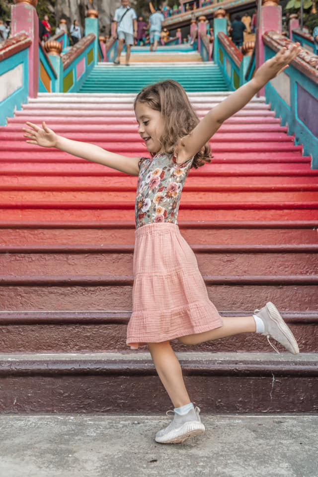 A young girl dances on the colorful steps of the Batu Caves in Malaysia, one of the best places to visit in Asia with kids.