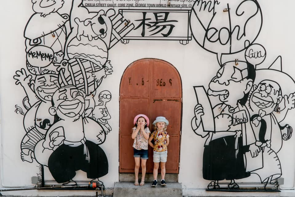 Two kids stand in front of a door surrounded by street art in Penang Island, one of the best places to visit in Asia with kids.