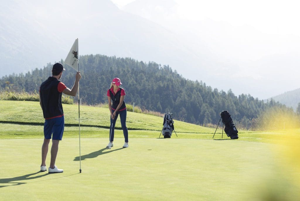 Two people golf at Kulm Hotel St. Moritz on a sunny day.