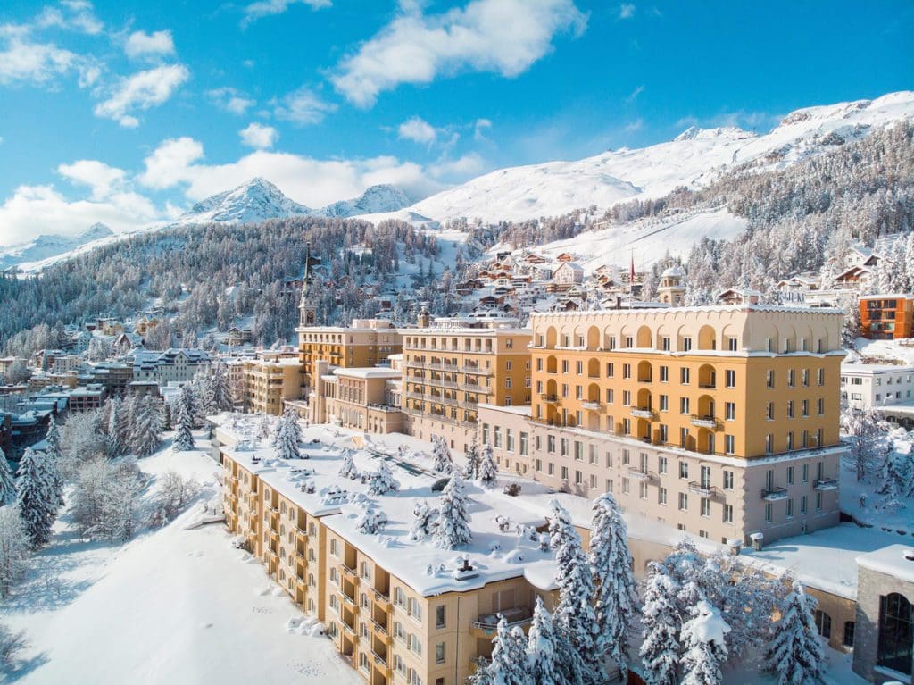 Kulm Hotel St. Moritz covered in snow, with snowcapped mountains in the distance.