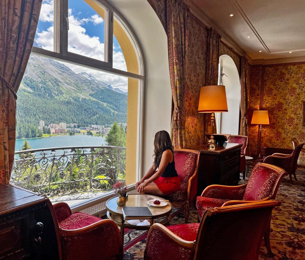 A woman looks out the grand windows of the lobby at Kulm Hotel St. Moritz onto a stunning view.