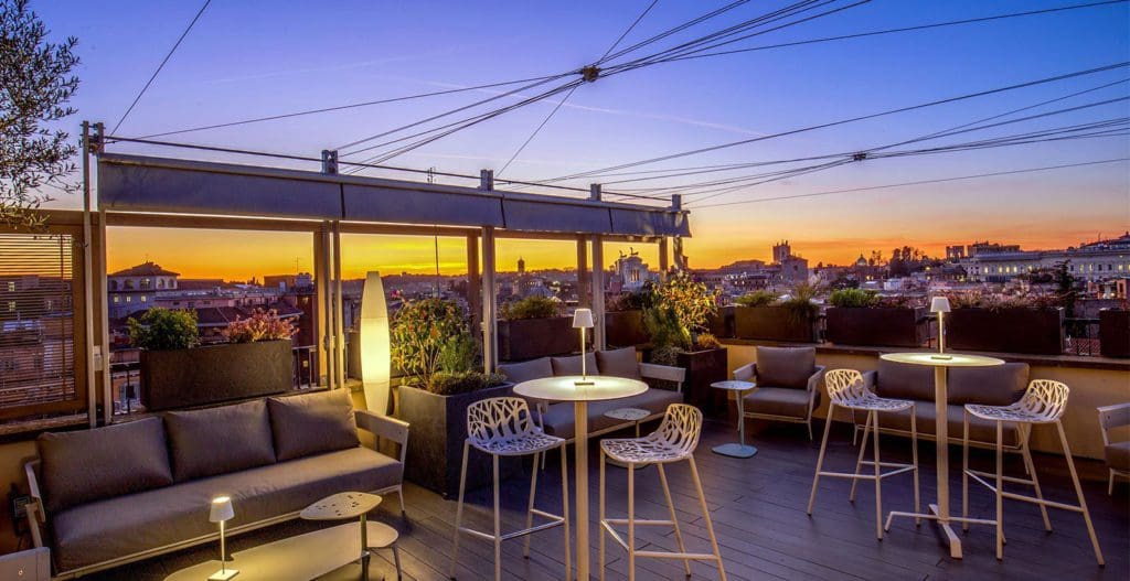 The rooftop terrace with a view of the city at Monti Palace Rome, with a sunset in the distance.