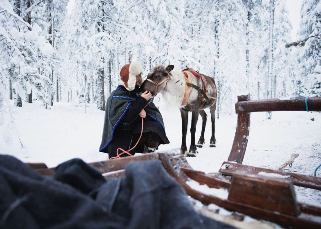 A man and a reindeer stand next to a sled in the winter.