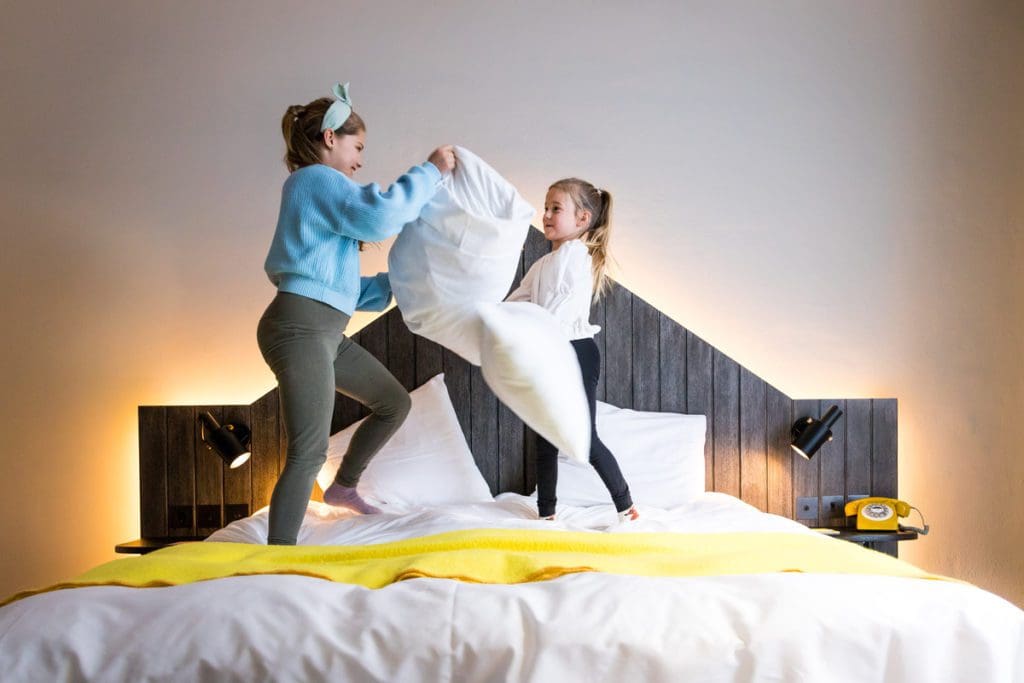 Two kids jump on a bed, while staying at Pulitzer Amsterdam.