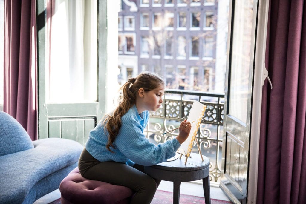 A young girl paints with natural light from a window in Pulitzer Amsterdam.