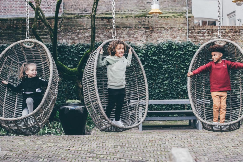 Three kids swing on outdoor swings at Pulitzer Amsterdam, one of the best hotels in Amsterdam for families.