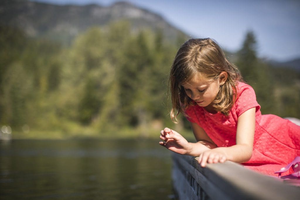 A young girl peers into a lake near Whistler, with mountains in the distance.
