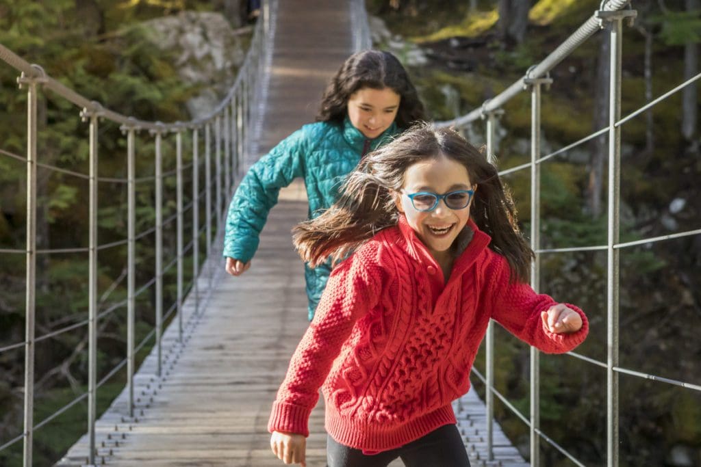 Two kids run across a bridge, while hiking near Whistler.