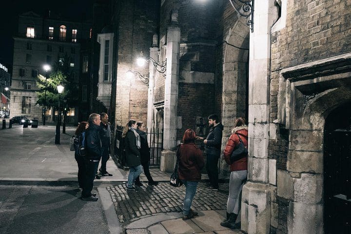 A tour guide leads a group of people on a ghost and ghouls tour of London at night.