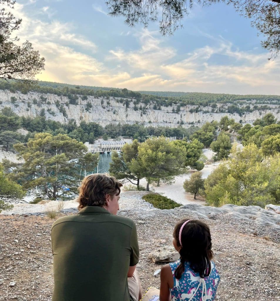 A dad and his young daughter sit outside, enjoying a scenic view of Cassis.