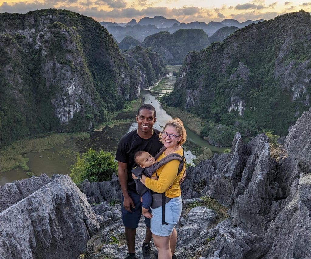 A family of three stands atop a mountain above a valley in Vietnam, one of the best places to visit in Asia with kids.