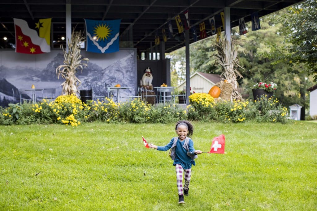 A young girl runs through a grassy area waving Swiss flags near a museum in New Glarus, Wisconsin.