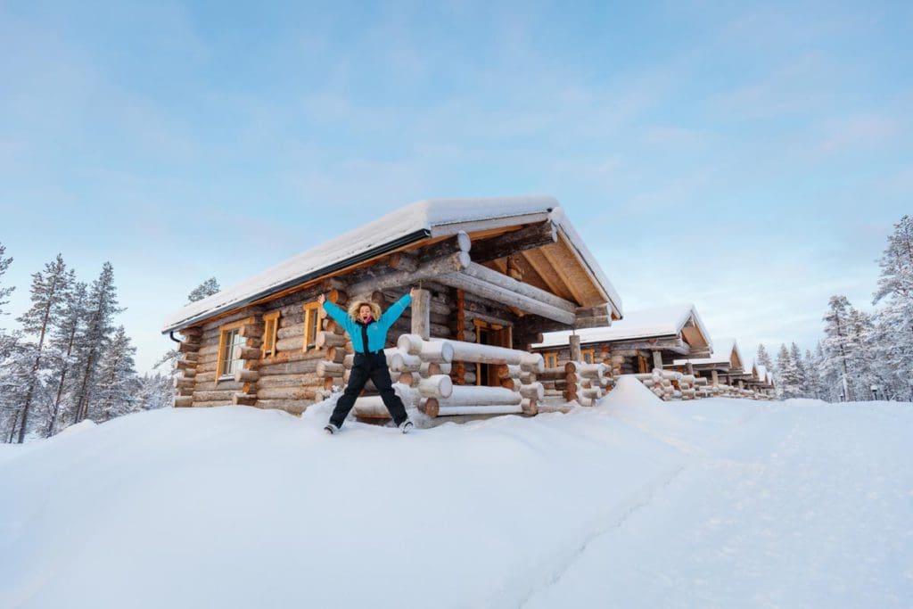 A woman stands excitedly in front of her cabin at Wilderness Hotel Muotka, one of the best Finland hotels for families.