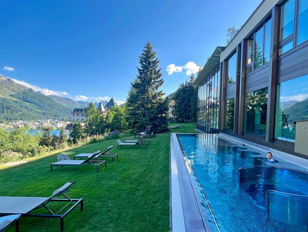 A young boy swims in the outdoor pool at Kulm Hotel with a view of the mountains, one of the best hotels in St. Moritz for families.