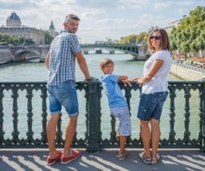 A family of three stands together along the River Seine in Paris.