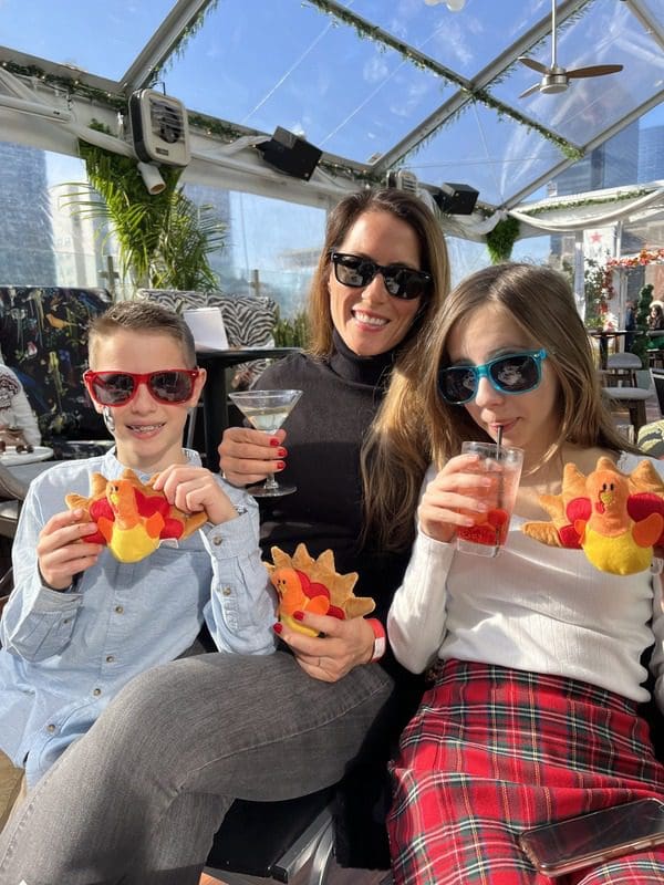 A mom and her two young kids sit on a rooftop terrace watching the Macy's Day Parade.