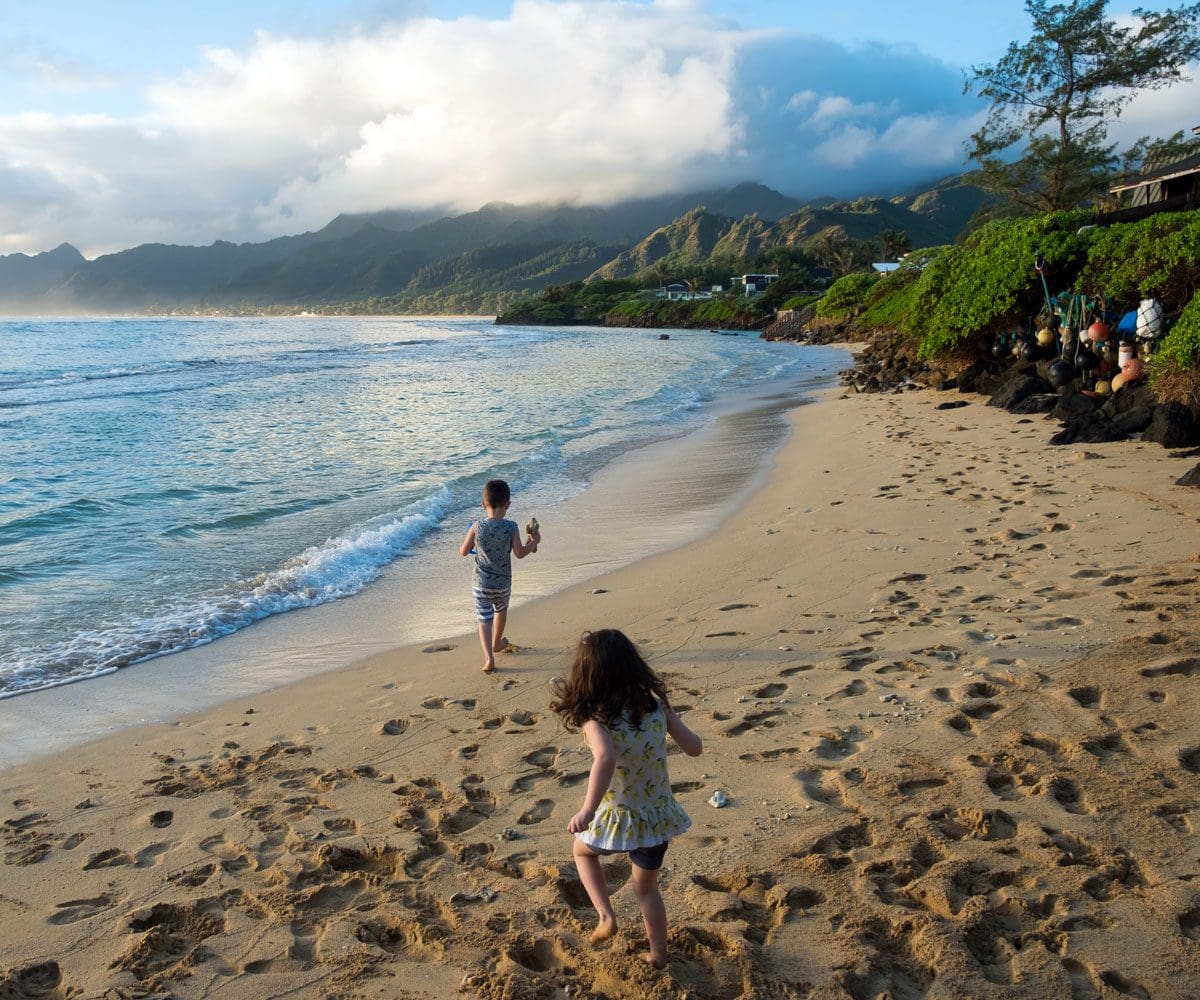 Two kids run along a beach in Hawaii on a sunny day.