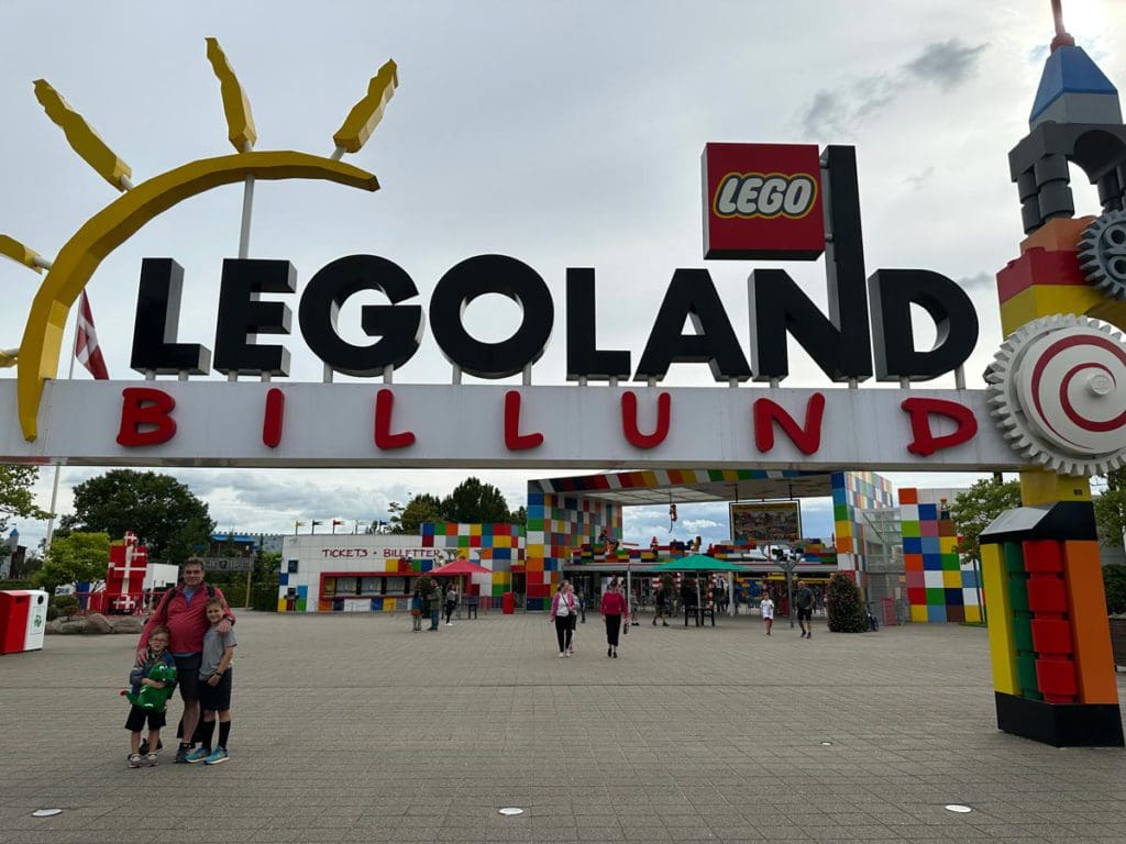 A dad and his two sons stand in front of the entrance sign to LEGOLAND® Billund Resort.