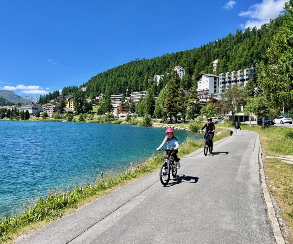Two kids bike along a path near Lake St. Moritz.