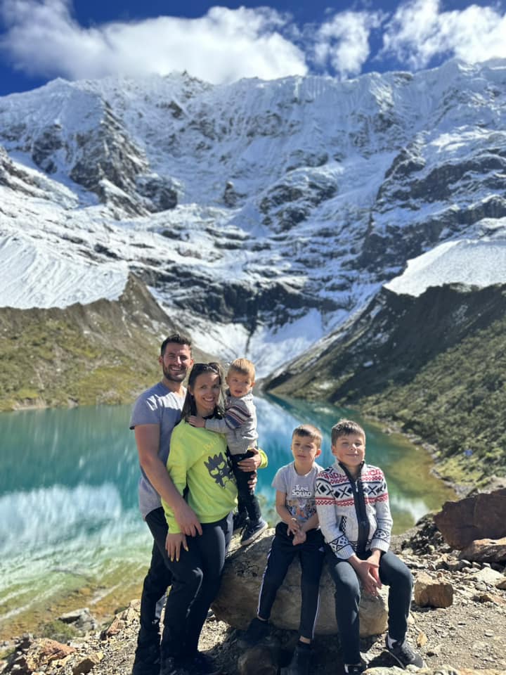 A family sits together with Lake Humantay in the distance.