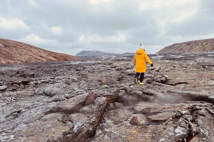 A woman in a yellow coat meanders along a hiking area while on the Fagradalsfjall Volcano Eruption - Custom Private Tour, No Group.
