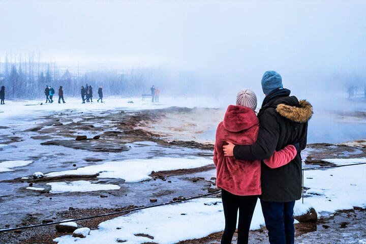 A couple stands together looking at a geyser on the Golden Circle, Fridheimar Farm & Horses Small Group Tour from Reykjavik.