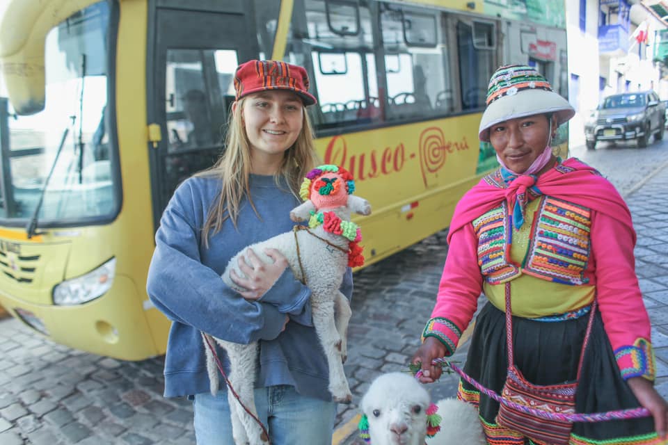 A young girl holds a baby alpaca, while exploring a market in Cusco, Peru.