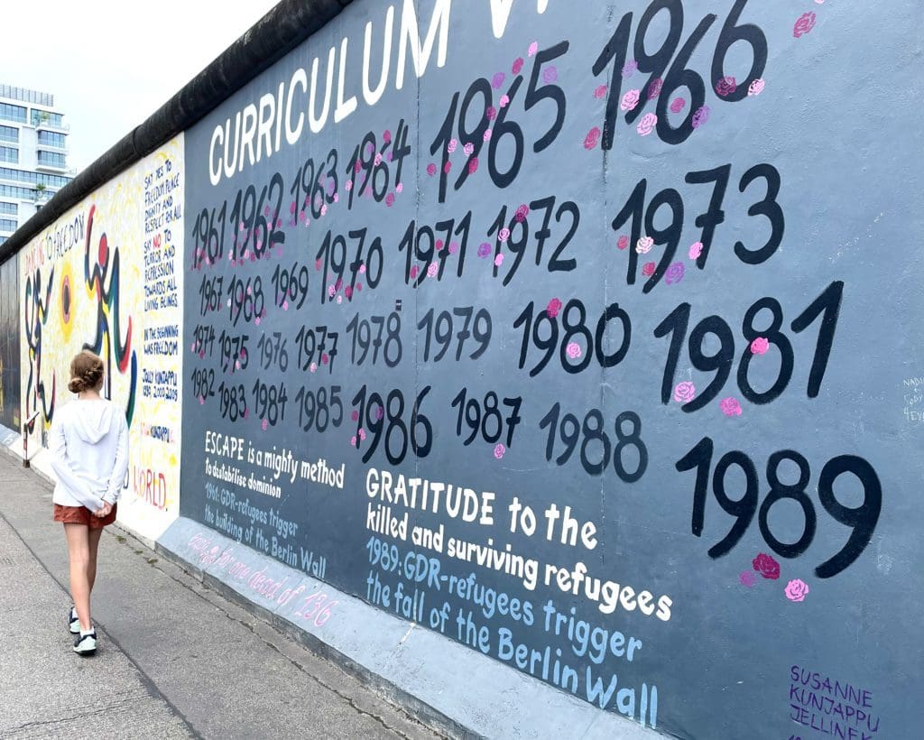 A young girl walks along an outdoor mural in East Germany.