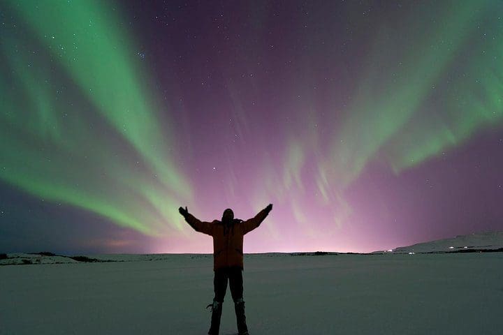 A man stands under the northern lights on the Northern Lights Tour from Reykjavik, one of the best Iceland tours with kids.