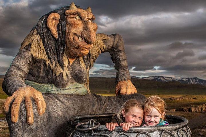 Two kids pose under a wooden troll on the Reykjavik Folklore Walking Tour: Meet the Elves, Trolls & Ghosts of Iceland.