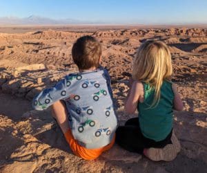 Two kids sit atop a cliff with a view of Valle de la Luna Atacama below.