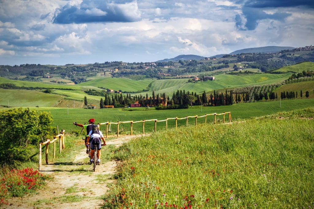 Two people bike in the Tuscan countryside. Taking a day trip from Tuscany is one of the best things to do on a Florence itinerary for families! 