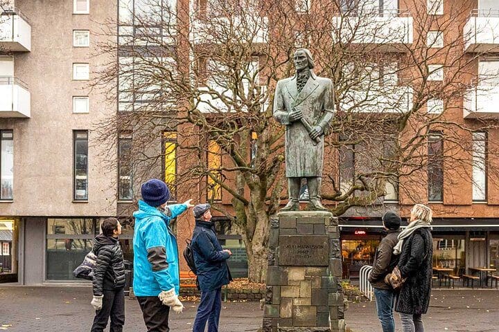 A tour guide shows people a statue, while on the Walk with a Viking: Private Tour of Reykjavik's Top Sights and Local Spots.