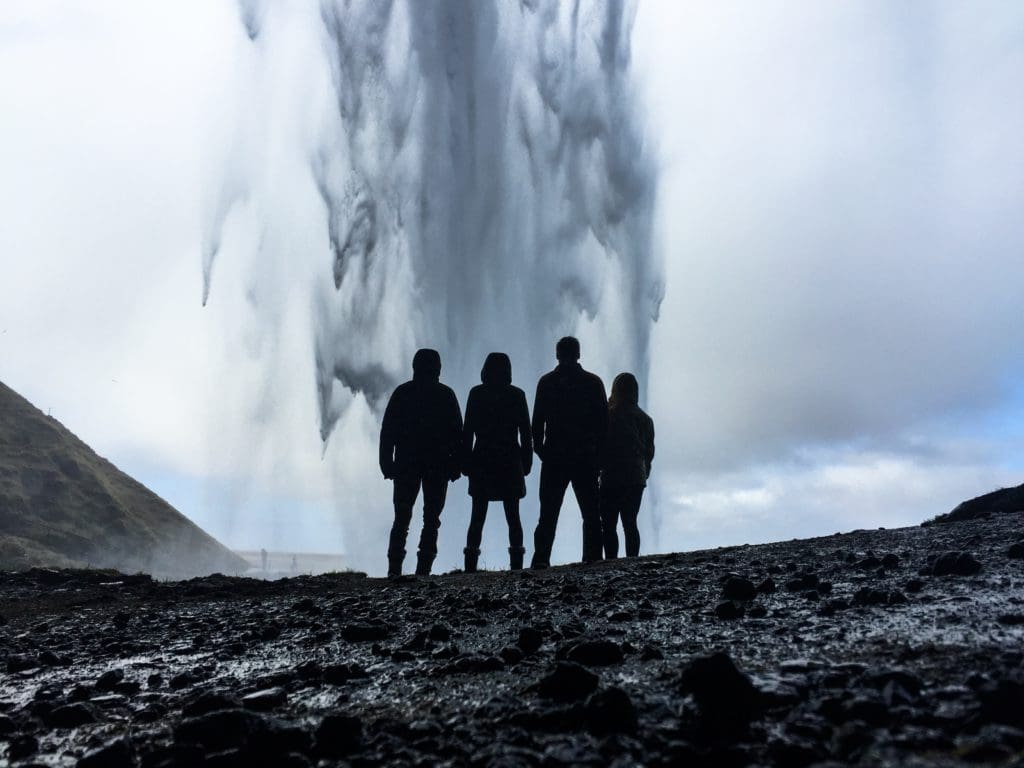 Four people stand together looking at Seljalandsfoss waterfall in Iceland.