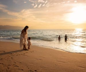 A mom and her young children walk along a beach in Puerto Vallarta at sunset.