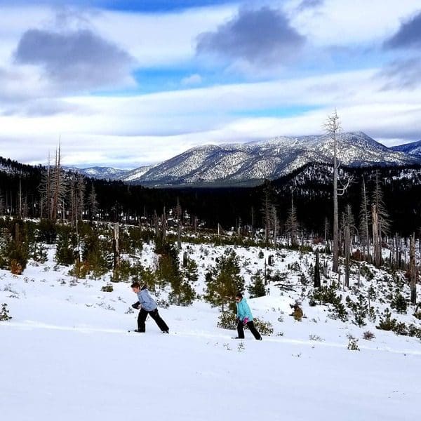 Two kids trek across the snow in snowshoes on a trail in Lake Tahoe, one of the best things to do while on a ski vacation to Lake Tahoe with kids.