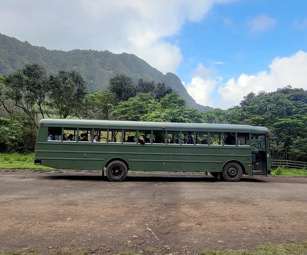 A bus sits parked at Kualoa Ranch & Private Nature Reserve, with mountains in the distance.