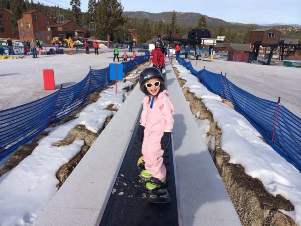 A young girl stands on a magic carpet lift while skiing in Lake Tahoe.