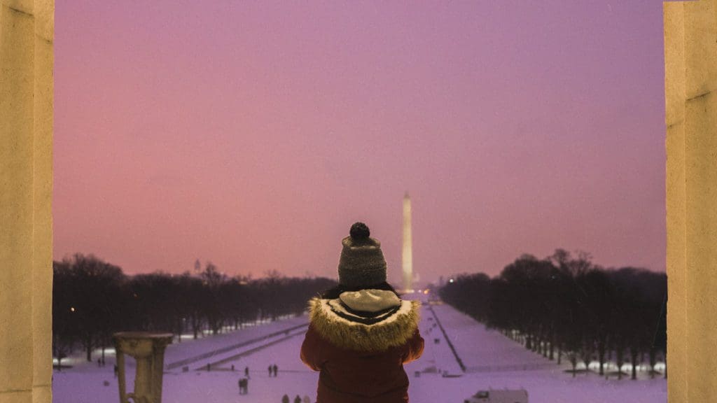 A young boy wearing a winter coat looks out at the Washington Monument in DC, one of the best budget-friendly Christmas destinations in the US for families.