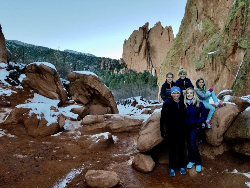 A family of five sits amongst a light snowfall in Garden of the Gods near Colorado Springs, one of the best places to visit on a Denver itinerary for families!