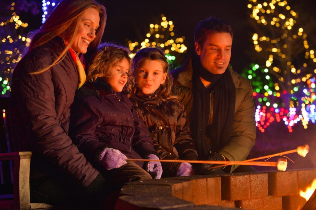 A family of four roasts marshmallows, surrounded by Christmas lights, in Asheville, one of the best budget-friendly Christmas destinations in the US for families.