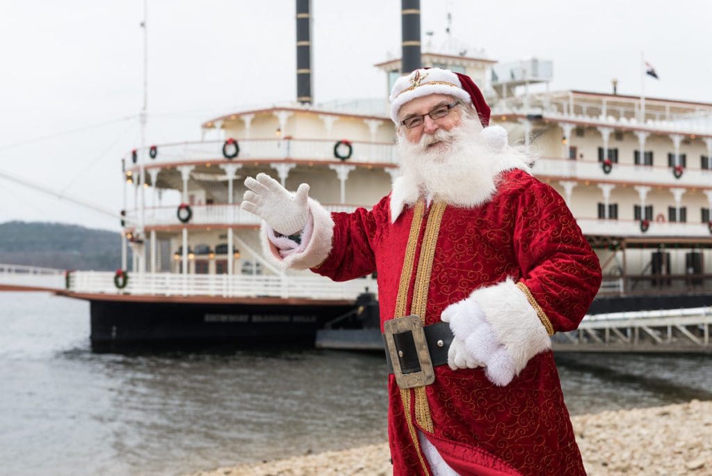 Santa stands in front of a river cruise boat about to embark on a holiday cruise in Branson, one of the best budget-friendly Christmas destinations in the US for families.
