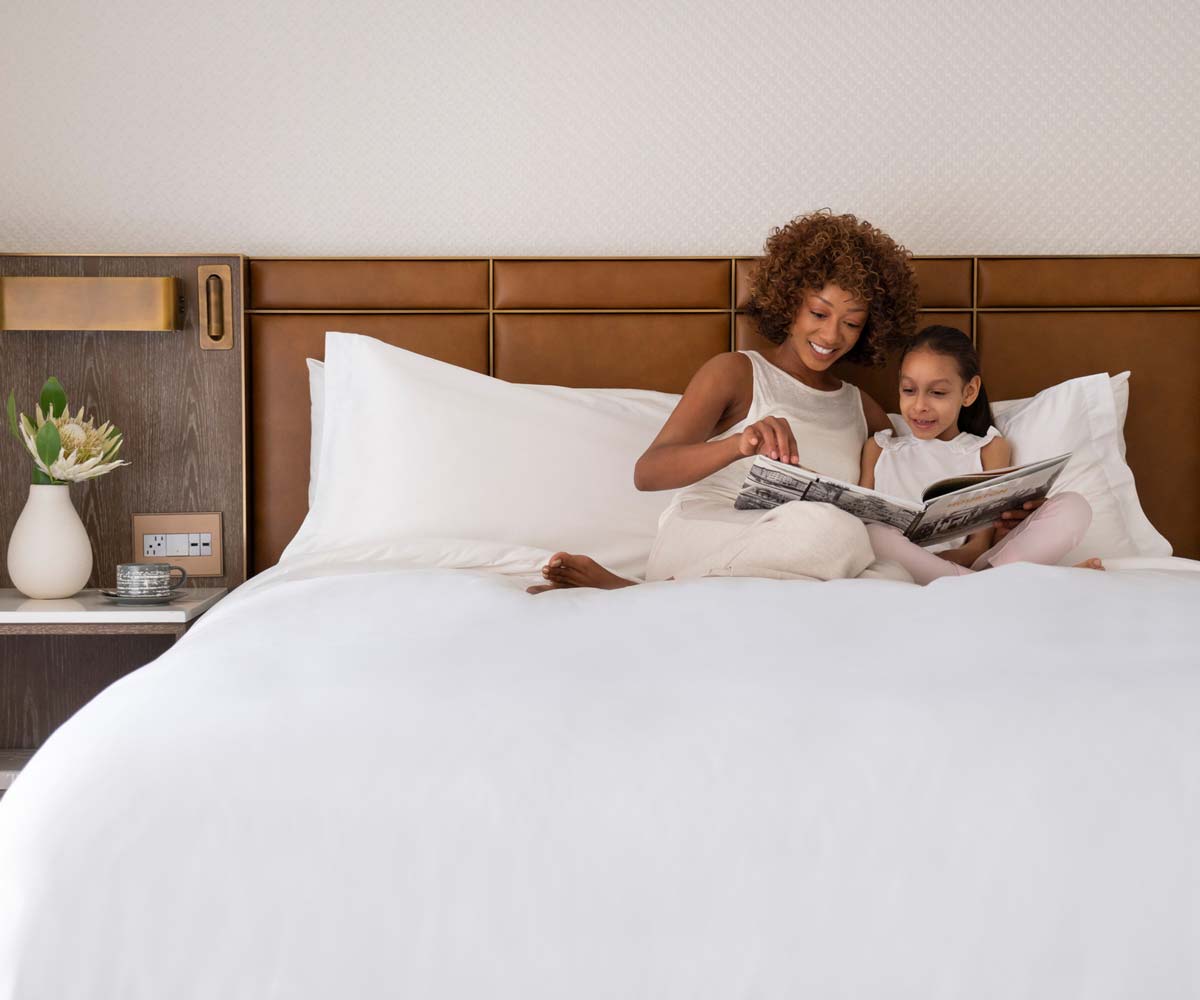 Mother and daughter cuddle up and read a book together, while staying at the Four Seasons Hotel Houston.