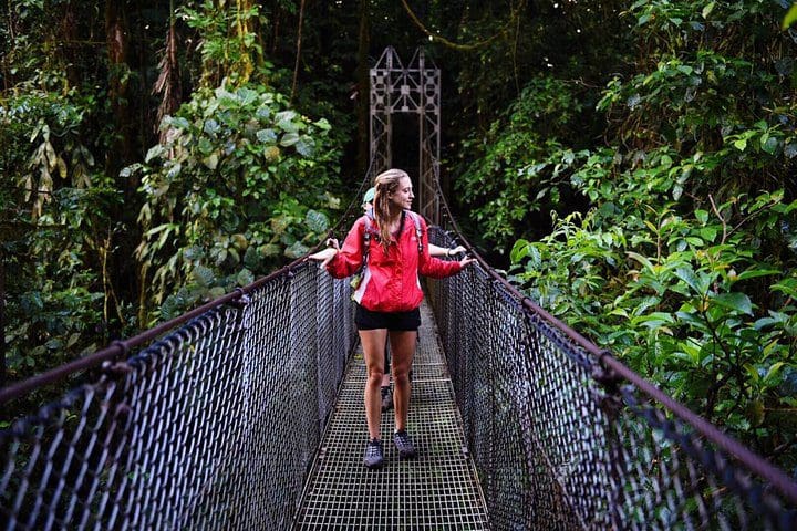 A girl walks along a swing bridge on the Full-Day Arenal Volcano, La Fortuna Waterfall and Hotsprings tour.