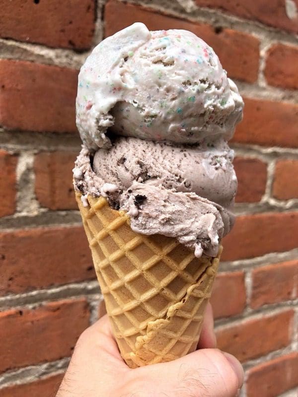 A hand holds out an ice cream cone from Ice Cream Riot, one of the best dessert spots in Denver with kids.