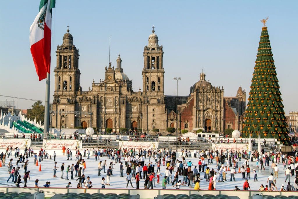 People ice skating at a rink in Mexico City with a huge Christmas tree nearby.