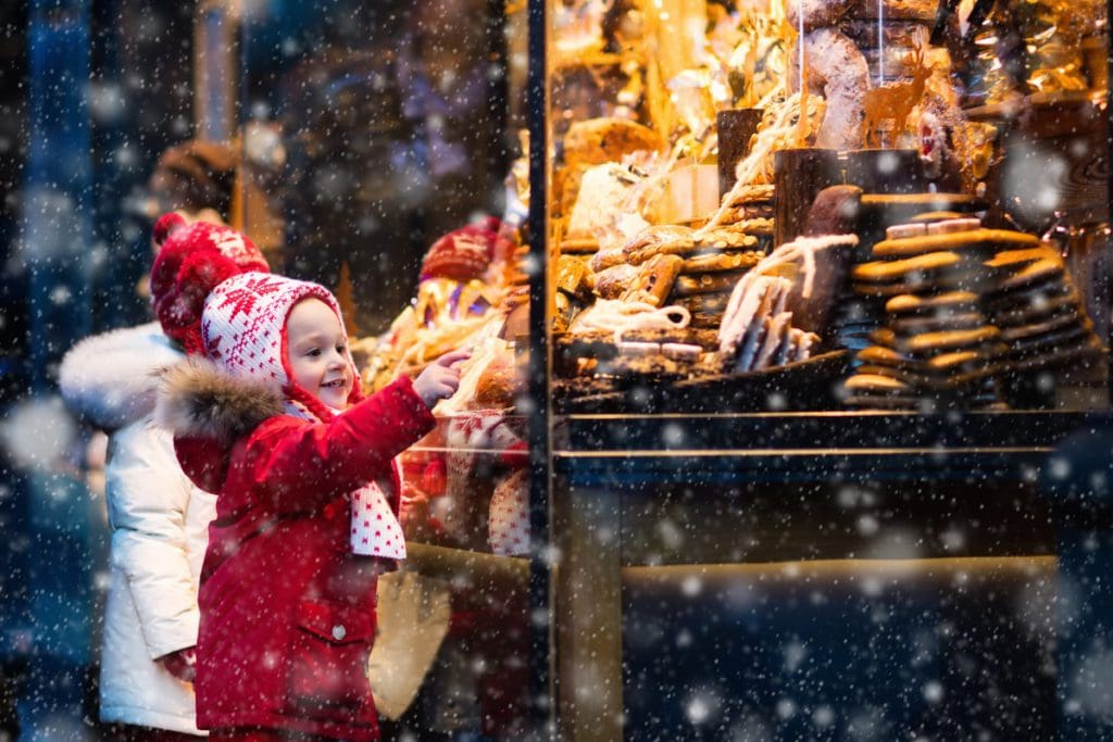 A young child wearing red, looks at Christmas treats through a window, while exploring Munich.