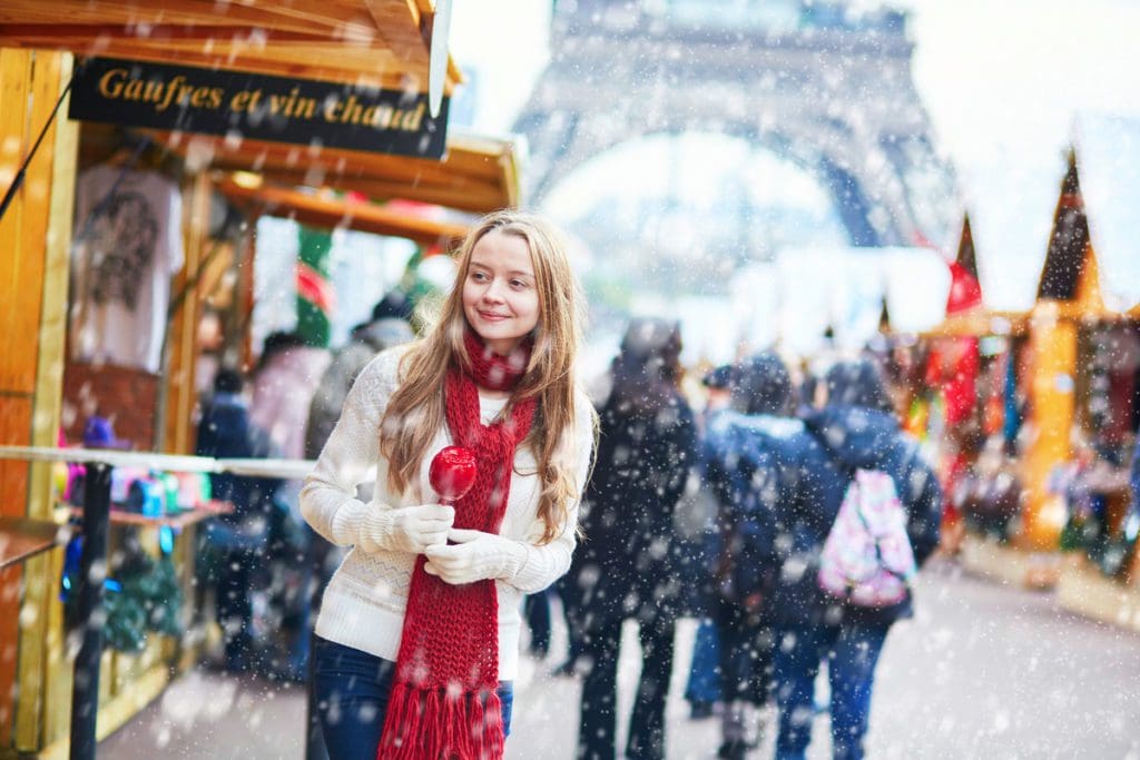 A young girl enjoys a Christmas market in front of the Eiffel Tower in Paris, one of the best places for Christmas for families in the world.