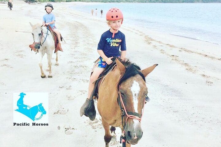 Kids ride horses along a beach on the 1.5 Hours Private Horseback Riding Tour in Playa Conchal.