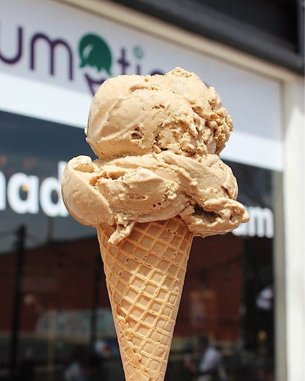 An ice cream cone in front of the sign for Scrumptious Ice Cream and Candy Shoppe.